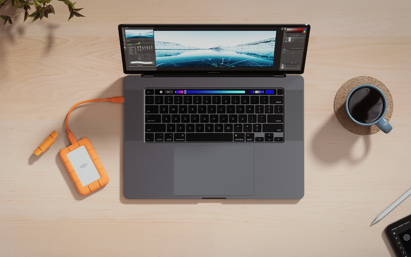 Overhead shot of a laptop computer plugged into a LaCie Rugged Mini SSD sits on a desk next to a cup of coffee.