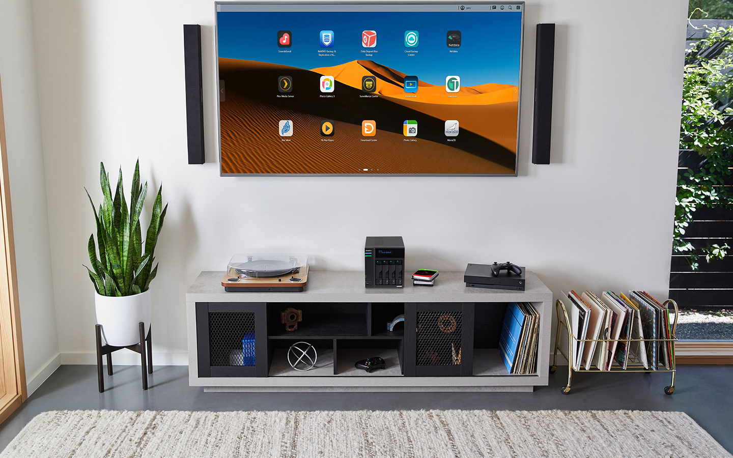 A large flatscreen with app icons hangs above an entertainment center holding a record player, NAS with IronWolf Pro drives, and Xbox.