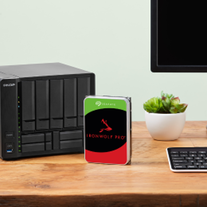IronWolf Pro drive positioned centrally on a desk is surrounded by a NAS system, computer screen, and keyboard.