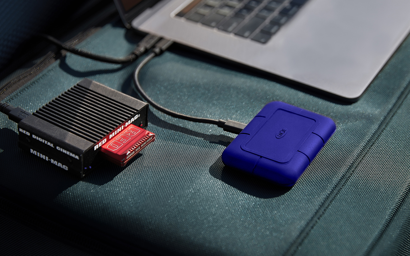 Blue LaCie Rugged Pro5 portable drive connected to a laptop sits next to an SSD card reader.