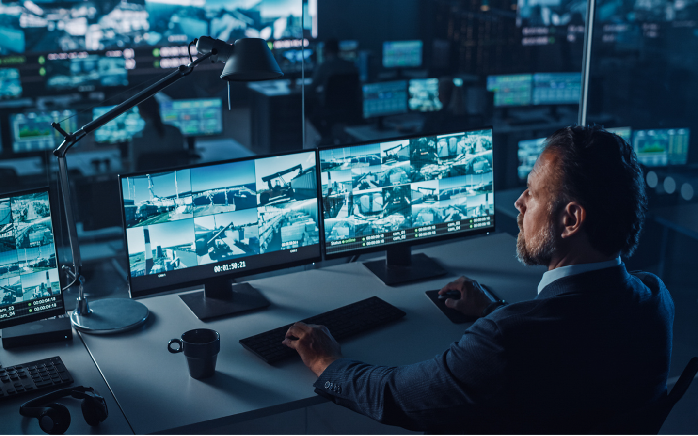 A businessperson monitors video surveillance feed screens in a corporate security department.