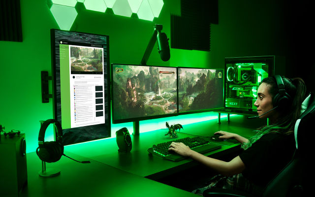 Person wearing headphones sits in front of four screens and a mic, playing a video game.