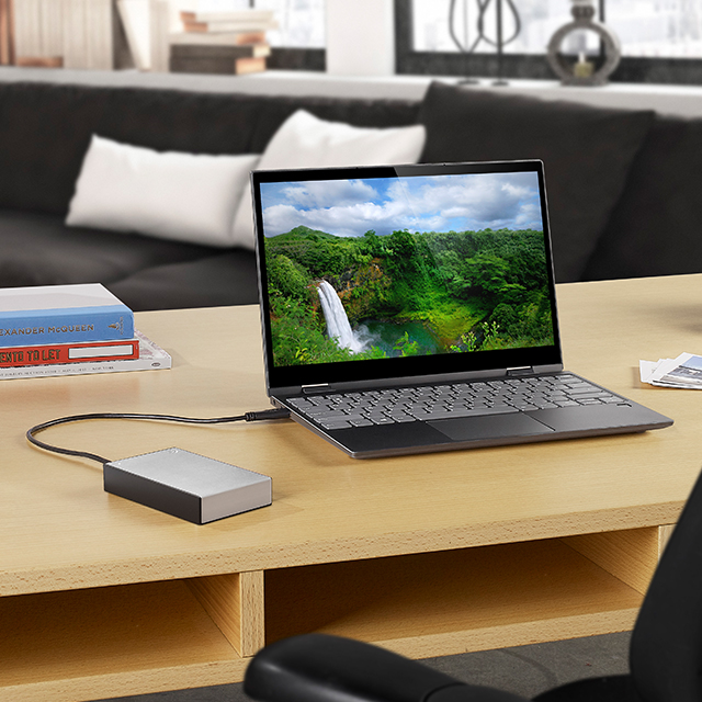 Laptop on a desk in a home office setting is plugged into a silver portable Seagate One Touch external drive.
