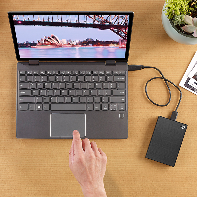 Overhead view of a person using a laptop connected to a black Seagate portable external drive.