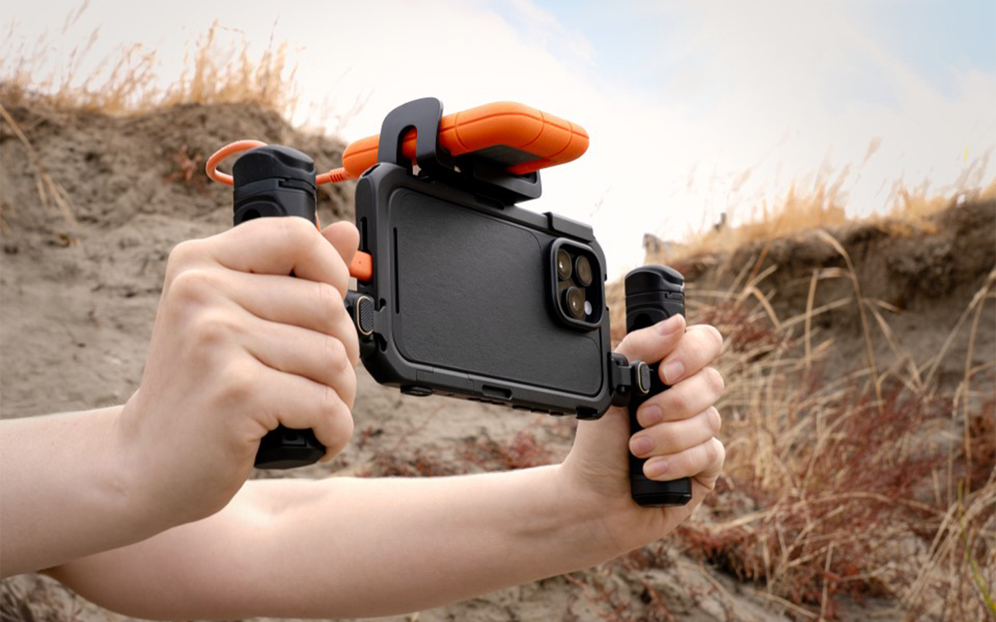 Person holding phone on stabilizer outdoors; LaCie Rugged SSD4 attached.