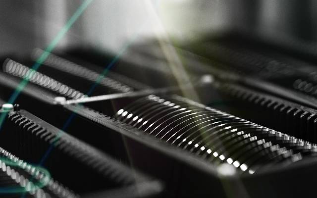 Close-up of semiconductor wafers arranged in a cleanroom storage rack, illuminated by light reflections and lens flares.